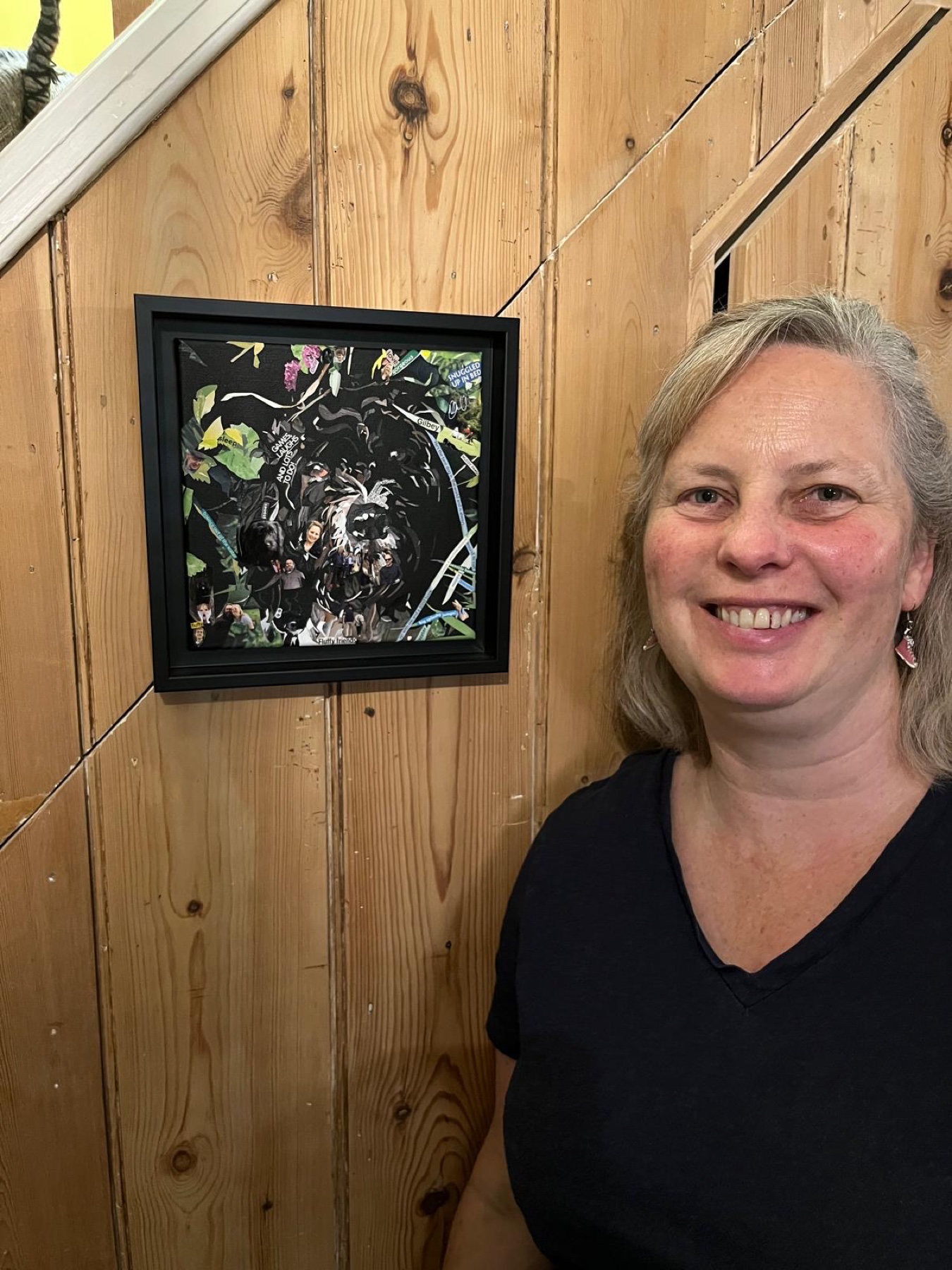 Artist Tiggy beside a framed collage pet portrait on the stairs